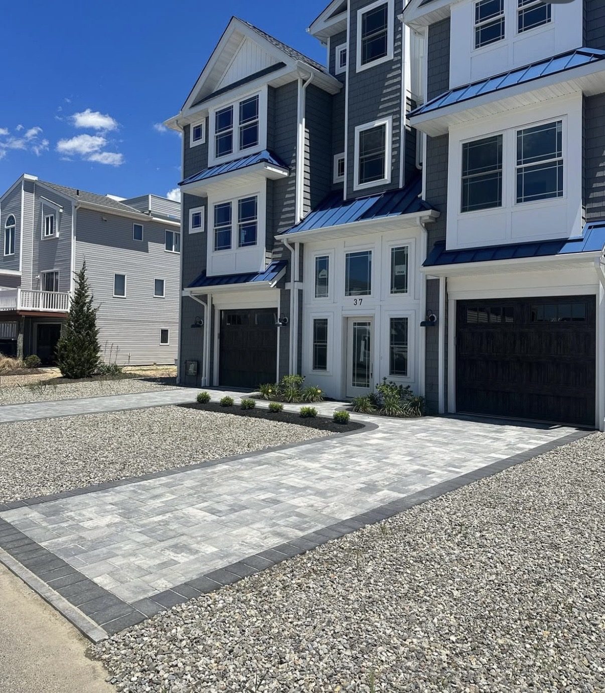 New three-story shore home with blue standing-seam roofs and paver driveway