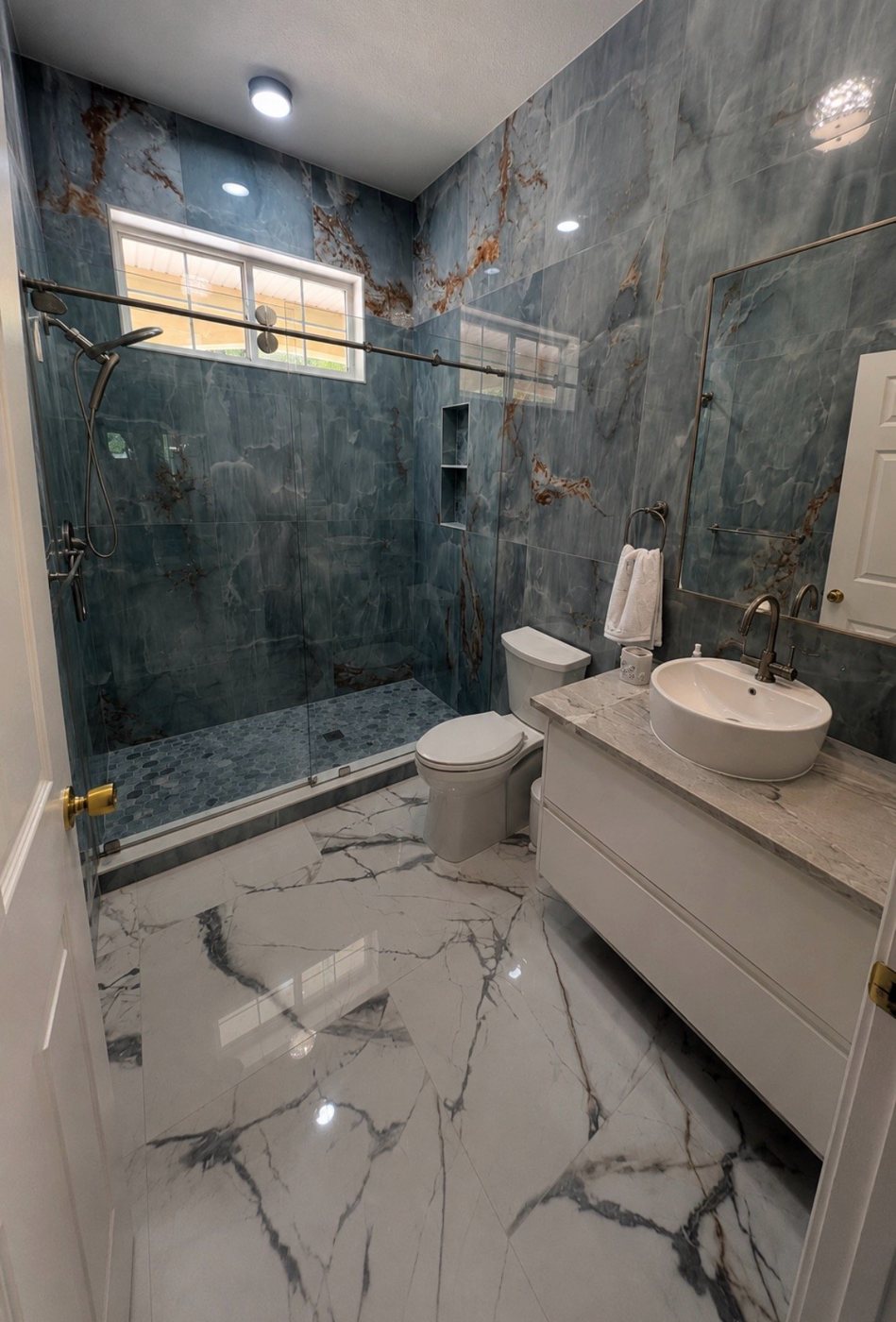 Renovated bathroom with blue marble-look tile, glass shower and floating vanity